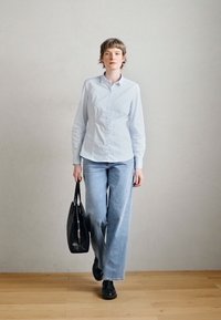 Svetlomodrá košeľa s dlhým rukávom, vysoko pásové modré džínsy, čierna kabelka a topánky. Jednoduchý dizajn, mäkká textúra, ležérny strih.