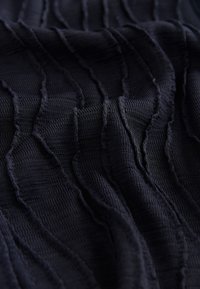 Dunkelblauer Stoff mit einem texturierten, wellenförmigen Muster, das erhöhte horizontale Linien und eine weiche, leicht gekräuselte Oberfläche aufweist.