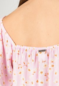 Blusa floral rosa claro com decote elástico, apresentando pequenos padrões de flores laranja e amarelo e uma etiqueta da Billabong perto da costura.