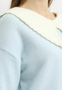 Suéter de punto azul claro con un acabado texturizado, que presenta un cuello blanco con un borde en forma de concha. La tela parece suave y acogedora.