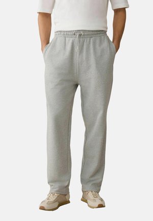 Mann trägt hellgraue Jogginghose mit elastischem Bund und Kordelzug, kombiniert mit beigefarbenen Sneakern und weißem Langarmshirt.