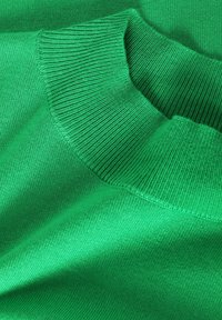 Gros plan d'un pull en maille vert avec un col roulé côtelé plié et un tissu à texture lisse.
