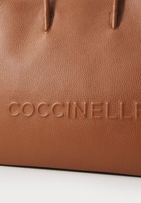 Brown leather handbag featuring a textured surface, two handles, and embossed "COCCINELLE" logo on the front.