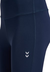 Granatowe legginsy wykonane z elastycznego materiału z wysokim stanem, z białym logo w wzór chevron na lewym udzie oraz szwami flatlock.