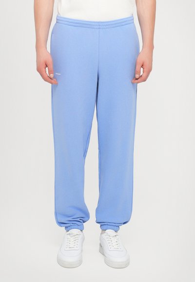 Light blue sweatpants made of soft fabric with an elastic waistband and cuffed hems, paired with white sneakers. Minimal logo detail present.