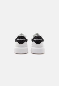 Paire de baskets blanches avec semelles épaisses et languettes de talon noires texturées affichant le nom de la marque "KARL LAGERFELD" en texte blanc.