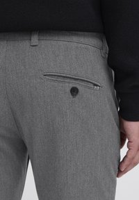 Sive krojene hlače z zadnjim žepom in zapiranjem na gumb. Material ima gladko teksturo in subtilen tkan vzorec.