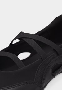 Chaussure décontractée noire avec des bandes élastiques croisées et des panneaux latéraux texturés, conçue pour le confort et un maintien sûr.