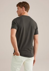 Camiseta de manga corta gris oscuro con cuello redondo, hecha de material de algodón, combinada con pantalones de color claro, vista desde atrás.