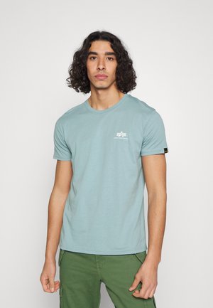 Hellblaues Baumwoll-T-Shirt mit rundem Ausschnitt und kurzen Ärmeln. Verfügt über ein kleines weißes Logo auf der oberen linken Brust und ein Etikett am Ärmel.