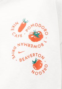 Κείμενο Nike Cafe με τρεις κόκκινες ντομάτες και ένα μικρό λογότυπο Nike σε λευκό ύφασμα, τοποθετημένα σε κυκλικό μοτίβο.