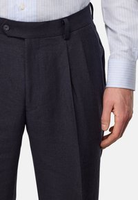 Pantalons plissés navy en tissu texturé, dotés d'une taille avec fermeture à bouton et passants de ceinture. Subtiles rayures grisâtres visibles.
