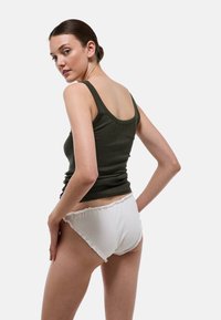 Haut débardeur côtelé vert olive associé à un slip hipster blanc à volants. Accent mis sur les textures des tissus et un design simple et ajusté.