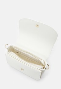 Vit läderhandväska med guldfärgad hårdvara. Funktioner inkluderar ett dragkedja-avdelning och en öppen yta, med en slät yta och rundad design.