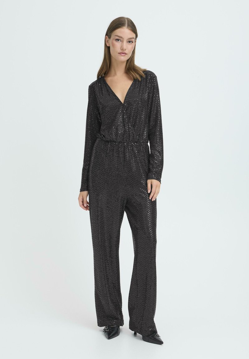 Czarny kombinezon z cekinami, z długimi rękawami i głębokim dekoltem w kształcie litery V. Posiada wyraźnie zaznaczoną talię i szerokie nogawki. Teksturowana, błyszcząca powierzchnia.