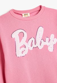 Roze sweatshirt met een ronde halslijn en ribgebreide manchetten. Bevat een sequentietekst "Baby" in het wit met paarse omranding. Zachte textuur.