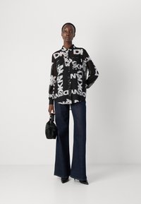Svart gjennomskinnelig skjorte med stor hvit "DKNY"-trykk, lange ermer, klassisk krage og to frontlommer; kombinert med brede mørk denimjeans.