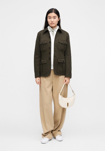 Olivno zelena jakna z večimi sprednjimi žepi, kombinirana s krem puloverjem, bež širokimi hlačami in majhno belo torbico. Bele superge.