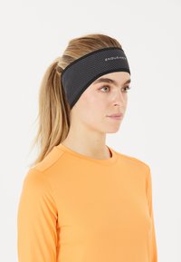 Svart hårband med prickig textur, med en logo, bärs av en person i en ljus orange långärmad topp.