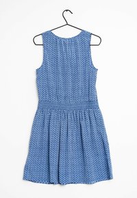 Robe sans manches bleue avec un motif géométrique, taille smockée et jupe plissée. Suspendue à un crochet en métal noir.