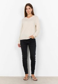 Maglione beige a scollo a V realizzato in tessuto morbido, abbinato a jeans neri slim. Modella che indossa tacchi a strappo con motivo a stampa leopardata.