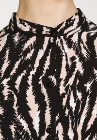 Svart och rosa kragskjorta med ett taggat, abstrakt mönster. Har knappar nedanför framtill, tillverkad av strukturerad tyg.