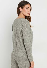Maglione grigio con texture, maniche lunghe, scollatura leggermente a barchetta e dettagli a costine sulle cuciture delle spalle. Il tessuto sembra morbido e informale.