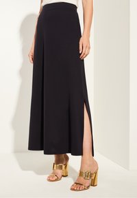 Svart maxiklänning med figurnära midja, sidoflikar och lätt tyg. Matchad med gyllene klacksandaler med breda spännen.