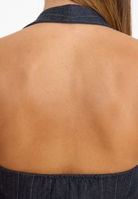 Rückansicht eines Kleidungsstücks mit Halterneck-Design, das ein dunkelgraues Fischgrätmuster aufweist und Haut am Rücken freilegt.