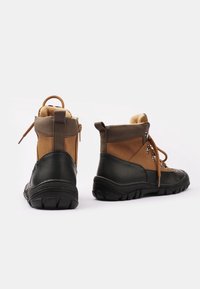 Botas de senderismo marrones y negras con una suela de goma texturizada, cuerpo de cuero, parte delantera con cordones, ojales de metal y un interior acolchado para mayor comodidad.