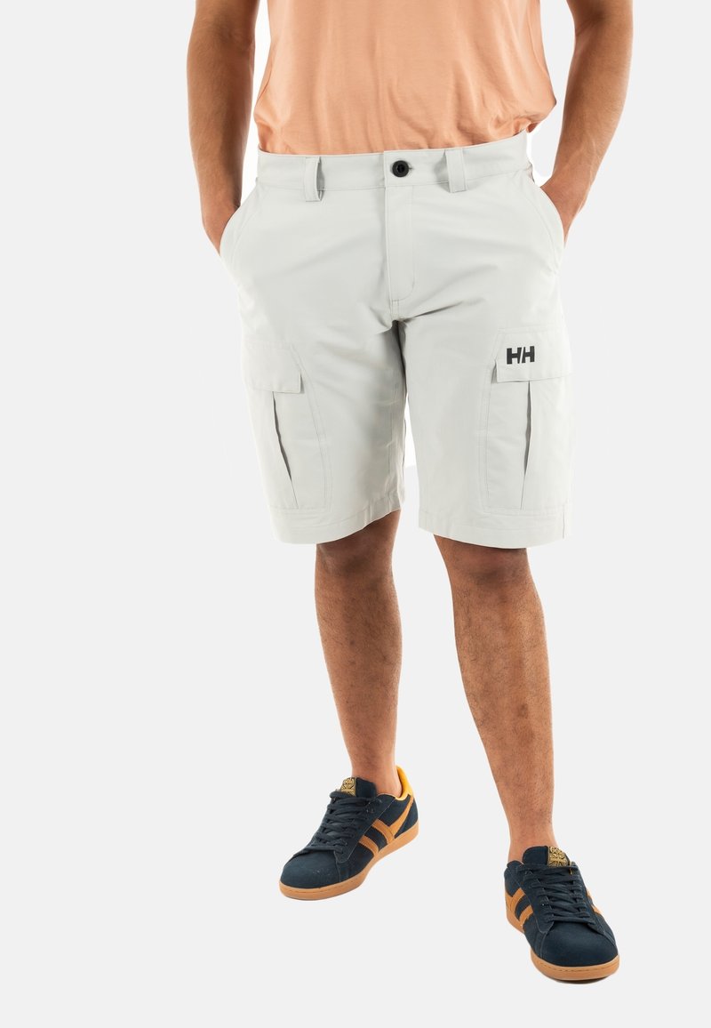 Pantaloni cargo grigi chiari con due tasche laterali, chiusura con bottone e logo "HH". Indossati con scarpe scure con dettagli arancioni.