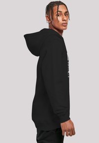 Black hoodie with a kangaroo pocket, adjustable drawstring hood, and white graphic design on the front. Model shown in side profile.