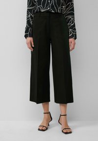 Zwarte wijde broek gemaakt van soepel stof, met een hoge taille, plooien en een gestructureerd silhouet, gecombineerd met zwarte sandalen met bandjes.