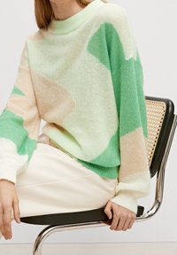 Sweter z przędzy w pastelowej zieleni, kremowym i beżowym kolorze z abstrakcyjnymi wzorami; charakteryzuje się okrągłym dekoltem i długimi, luźnymi rękawami. Gładka faktura.