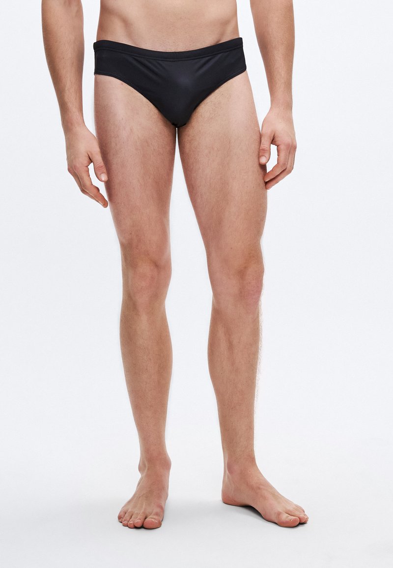 Cueca de banho masculina preta em tecido liso, com corte de cintura baixa e ajuste contornado. Estilo minimalista sem padrões visíveis.