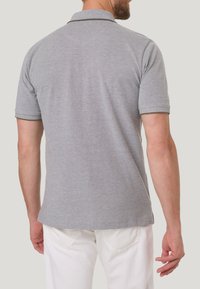 Grijze polo met een gestructureerde afwerking, voorzien van een kraag en contrasterende biezen. Draagt een relaxed fit met witte broek.