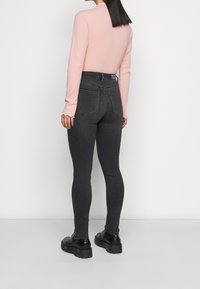 Vaqueros negros de cintura alta con un diseño ajustado y bolsillos traseros, combinados con una blusa de manga larga de canalé rosa pálido con bordes en forma de pico.