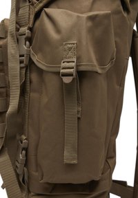 Gros plan sur la poche latérale d’un sac à dos en tissu marron avec sangle de sécurité et boucle en plastique, montrant une texture durable et des détails de couture.