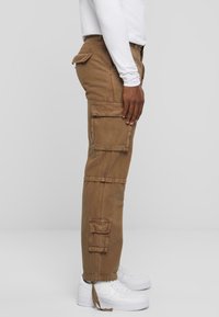 Pantalons cargo en tissu marron, dotés de plusieurs poches latérales/hanche, d'une coupe décontractée et de chevilles resserrées, associés à des baskets blanches.