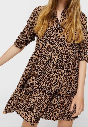 Femme portant une robe ample boutonnée avec des manches retroussées dans un motif léopard marron et noir.