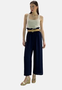 Navy wijde broek met een rimpel tailleband, gecombineerd met een crèmekleurig tanktop en gouden sleehaksandalen, met een geweven lichtbruine riem.