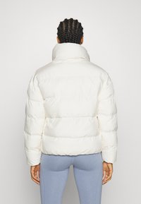 White puffer jacket with a high collar, quilted design, and visible stitching. Soft texture, short length, and oversized fit.
