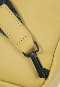 Cinghia di attacco per borsa impermeabile gialla, con clip metallica nera e cuciture rinforzate su una superficie liscia.