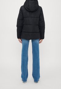 Svart puffjacka med huva, försedd med horisontell sömnad, kombinerad med blå vida jeans och vita sneakers.