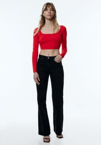 Rode cropped lange mouwen top met vierkante halslijn, gecombineerd met zwarte hooggetailleerde flared jeans en zwarte open-teen hoge hakken sandalen.