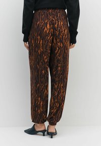 Hnedé nohavice s leopardím vzorom v tmavých a svetlých odtieňoch, s elastickým pásom a zúženými manžetami, skombinované s čiernymi mulemi.