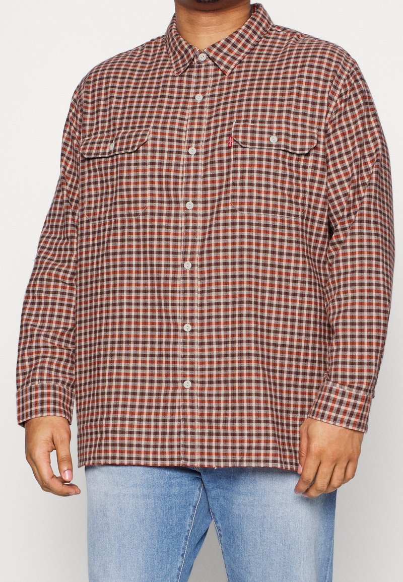 Camisa de cuadros roja y marrón con dos bolsillos en el pecho, mangas largas y cuello; hecha de una tela texturizada.