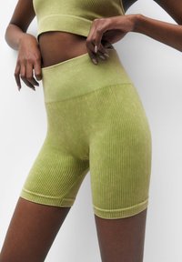 Shorts verts côtelés à taille haute, confectionnés dans un tissu doux et texturé avec des bandes élastiques. Le modèle présente une coupe ajustée et des ourlets sans coutures.