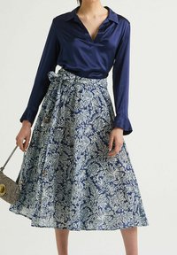 Blusa di raso blu con scollo a V e maniche lunghe abbinata a una gonna al ginocchio con un motivo floreale blu e bianco. Include una cintura.