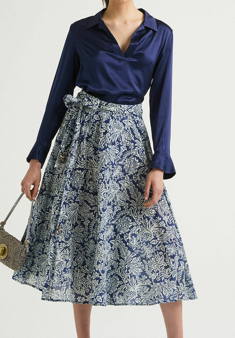 Blusa di raso blu con scollo a V e maniche lunghe abbinata a una gonna al ginocchio con un motivo floreale blu e bianco. Include una cintura.